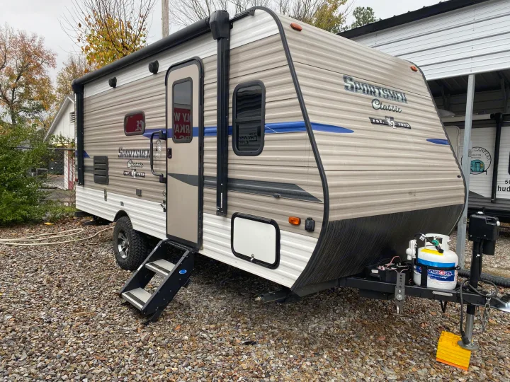 Sportsmen Classic travel trailer from Huddleston RV Rental. Grey/tan camper with blue accents, parked on gravel.. KZ Sportsman 2020