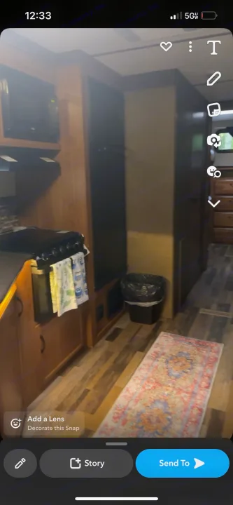 RV rental interior: A compact kitchen with stove, microwave, wood-look floor, and a colorful rug, hinting at cozy living.. Starcraft Travel Star 2016