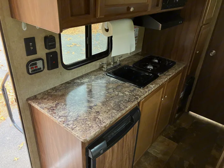 RV rental interior kitchen features a speckled countertop, black sink, and two-burner stove under overhead cabinets.. Forest River Viking 2016