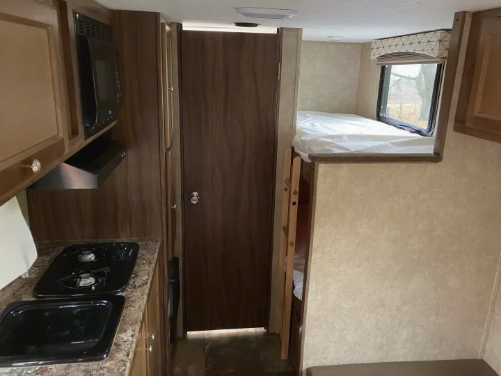This RV rental features a compact kitchen with stove, microwave, and a cozy bunk bed area.. Forest River Viking 2016