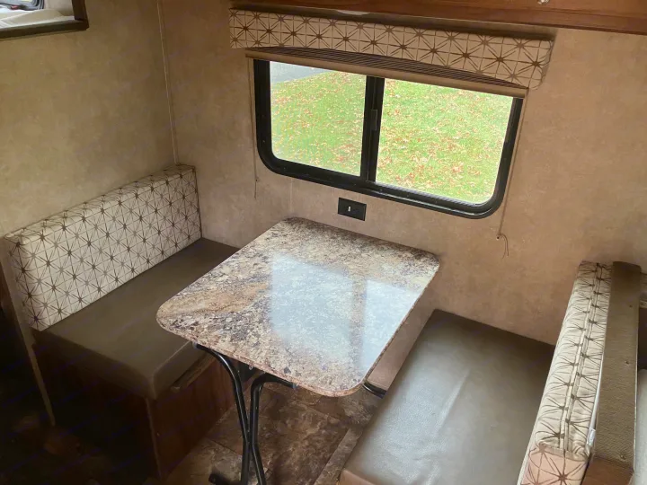 Cozy RV rental dinette area featuring patterned benches, a speckled table, and a window view of green grass.. Forest River Viking 2016