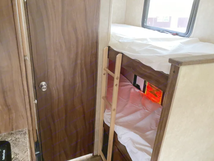 RV rental interior: bunk beds with white and orange bedding, a wooden ladder, and a dark wooden door. Ideal for families.. Forest River Viking 2016