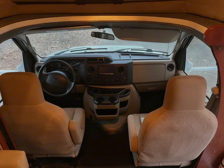 Inside an RV rental, showing the spacious cockpit with a Ford steering wheel, dashboard, and comfortable front seats.. Winnebago Winnebago 2014