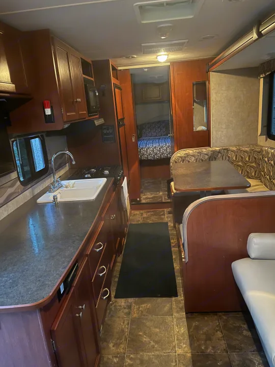 Inside an RV rental: full view of the compact kitchen, cozy dinette, and hallway to the bunk bedroom.. Winnebago Winnebago 2014