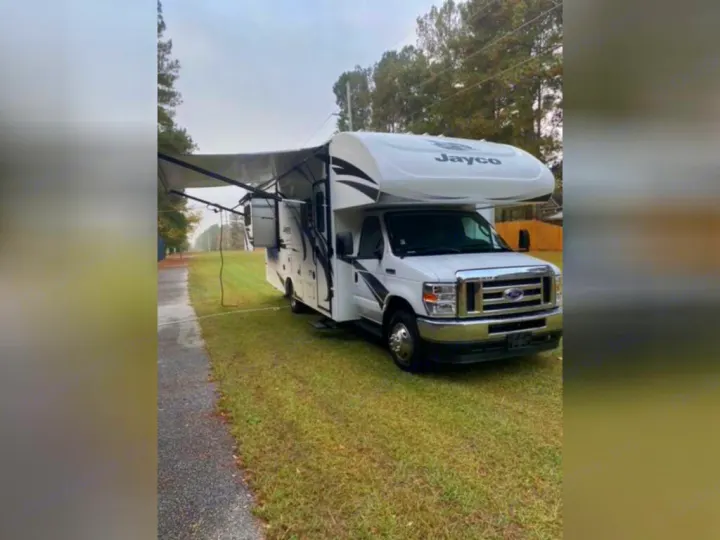 White Jayco Class C motorhome rv rental with awning out, ready for travel. Parked on green grass by a road.. Jayco Redhawk 2022
