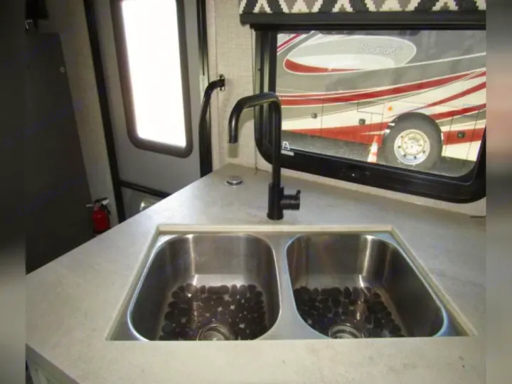 RV rental kitchen featuring a double sink, modern black faucet, and a view of another RV through the window.. Jayco Redhawk 2022