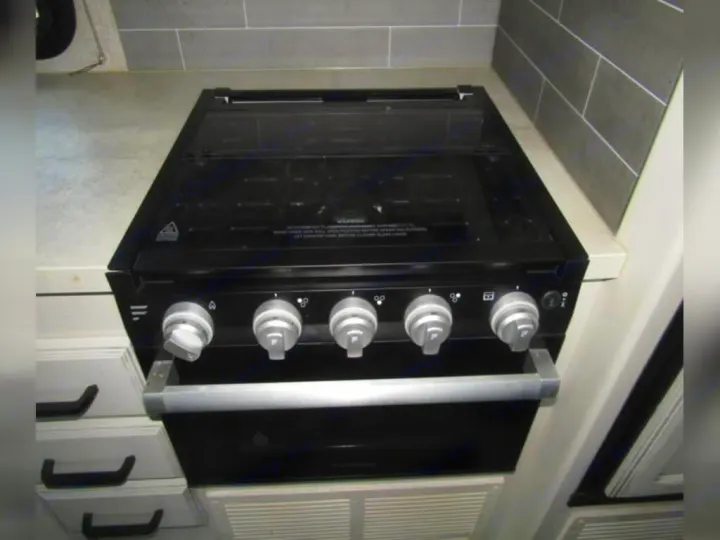 RV rental interior: Close-up of a sleek black stove/oven unit with five silver knobs and a handle, set in a light kitchen.. Jayco Redhawk 2022