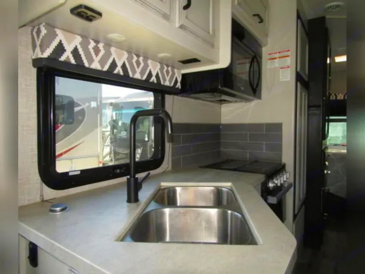 Modern rv rental kitchen with light gray countertops, double sinks, stove, microwave, and subway tile backsplash.. Jayco Redhawk 2022