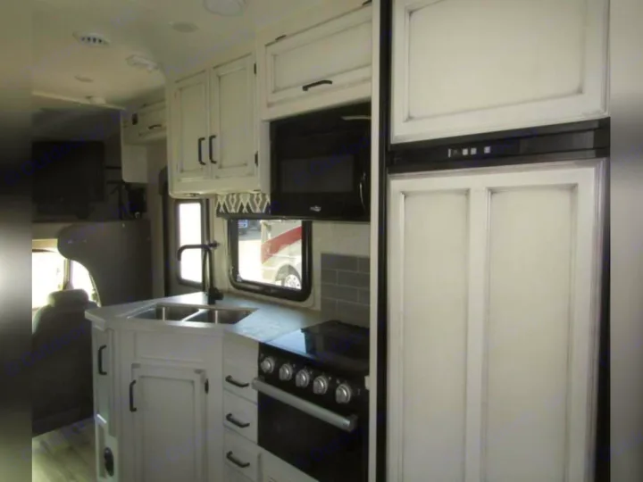 This rv rental features a compact kitchen with white distressed cabinets, black appliances, double sink, and paneled fridge.. Jayco Redhawk 2022