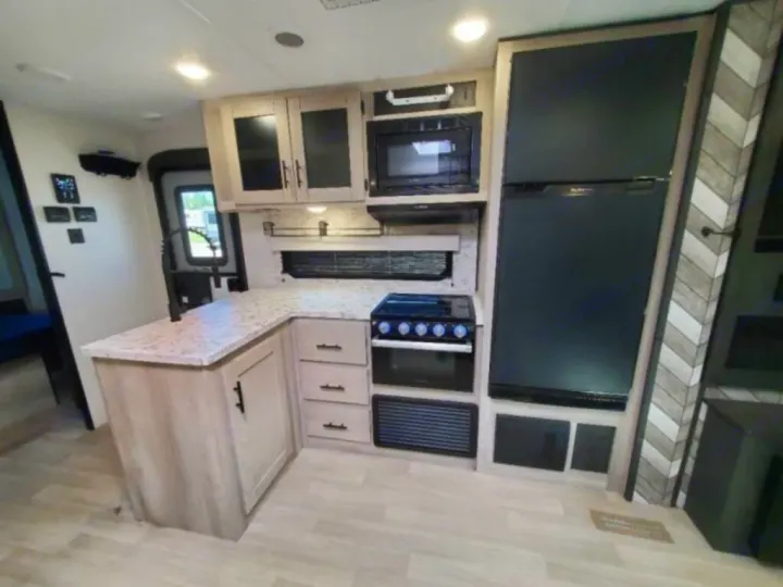 Modern RV rental kitchen featuring light wood cabinets, speckled counters, black appliances, and a full-size refrigerator.. KZ Connect C291BHK 2023