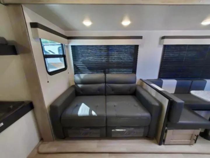 Inside this **rv rental**, a gray sofa sits next to a dinette with striped cushions, under windows with dark blinds.. KZ Connect C291BHK 2023