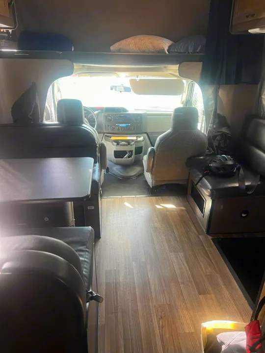 Spacious rv rental interior featuring the cockpit, a dining table, seating, and an over-cab bunk bed with pillows.. Thor Majestic 2019