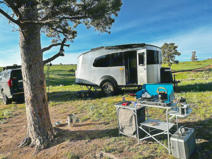 RV rental adventure: A modern trailer and SUV parked at a scenic campsite with an outdoor kitchen setup.. Airstream Basecamp 2023