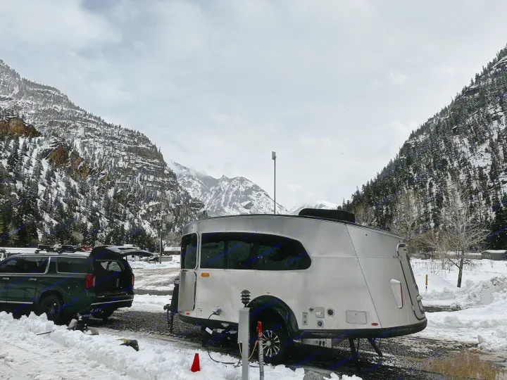 RV rental: Sleek silver travel trailer parked with an SUV at a snowy mountain campsite.. Airstream Basecamp 2023