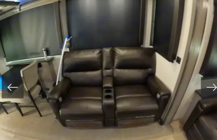 RV rental living area: brown recliner sofa with cup holders. Dark window blinds & small table visible. Cozy travel.. Keystone RV Montana 2021