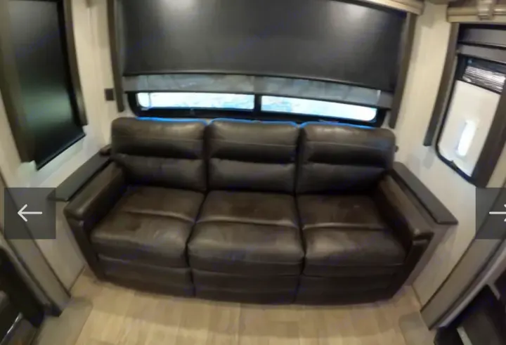 Comfortable RV rental living area with a dark three-seater recliner sofa and large windows with blinds.. Keystone RV Montana 2021
