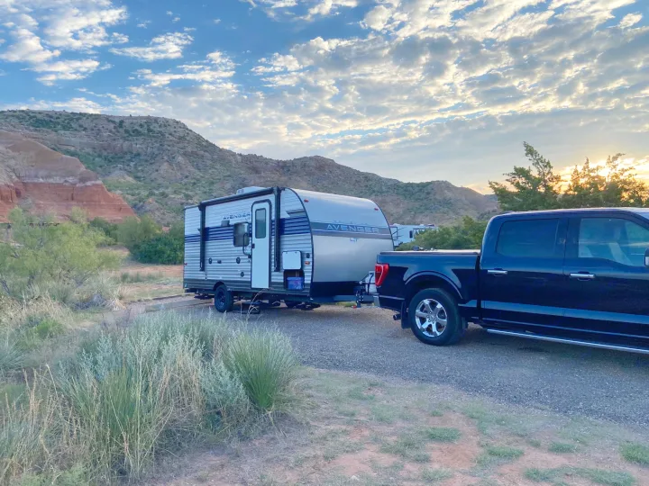 Scenic RV rental and truck parked at a desert campsite, with colorful mountains & a sunrise/sunset sky.. Avenger LT 2022