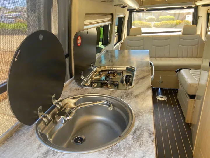 Inside an RV rental: a well-appointed kitchen with sink and two-burner stove, alongside comfortable cream-colored seating.. Airstream Interstate 2015