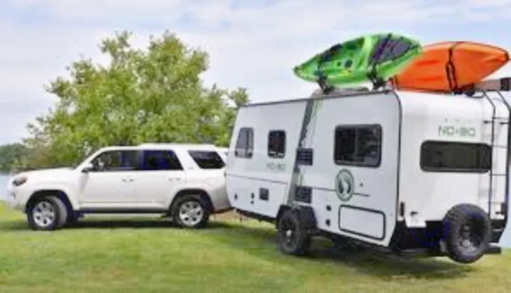 White SUV towing a sleek travel trailer with kayaks, ideal for an RV rental outdoor adventure. Perfect for camping trips!. Forest River No Boundaries 19.8 2021