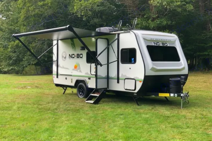 Compact white and black NO BO travel trailer RV rental with awning extended, parked on grass for outdoor adventures.. Forest River No Boundaries 19.8 2021