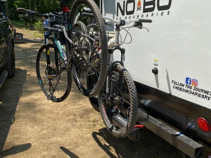 Rear view of an RV rental with three bikes on a hitch rack on a dirt campsite. Ready for outdoor fun!. Forest River No Boundaries 19.8 2021