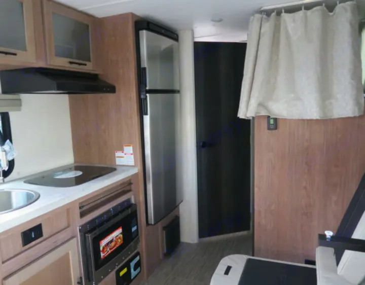 This RV rental interior showcases a compact kitchen with sink, stove, microwave, fridge, and curtained living area.. Forest River No Boundaries 19.8 2021