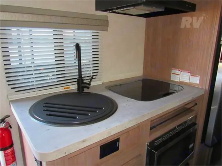 Compact RV rental kitchenette with a covered sink, modern black stovetop, and built-in microwave. Forest River No Boundaries 19.8 2021