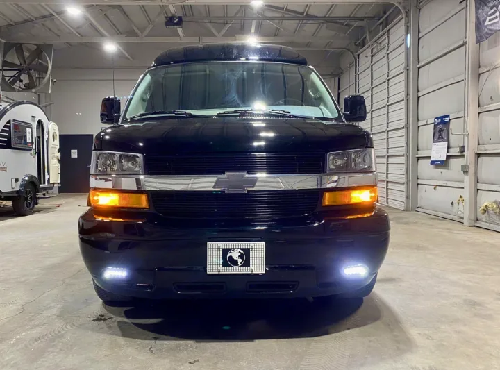 This black Chevrolet van and white teardrop camper offer great options for RV rental. Shown in a brightly lit showroom.. Passenger Van 9 Passenger Van 2024