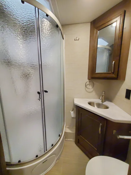 This RV rental bathroom features a textured glass shower, corner sink, mirrored cabinet, and toilet.. Entegra Coach Vision XL 2022