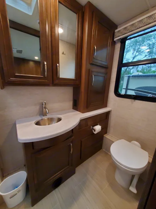 Well-appointed RV rental bathroom with a vanity, sink, toilet, mirrored medicine cabinets, and a window.. Entegra Coach Vision XL 2022