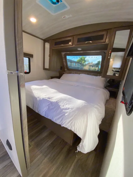Step into this bright RV rental bedroom, featuring a large bed with white bedding, overhead storage, and natural light.. Keystone RV Cougar 2022