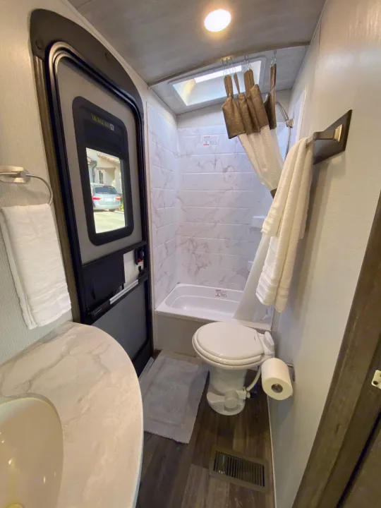 Inside a functional RV rental bathroom with a full shower, toilet, sink, and an exterior view from the door.. Keystone RV Cougar 2022
