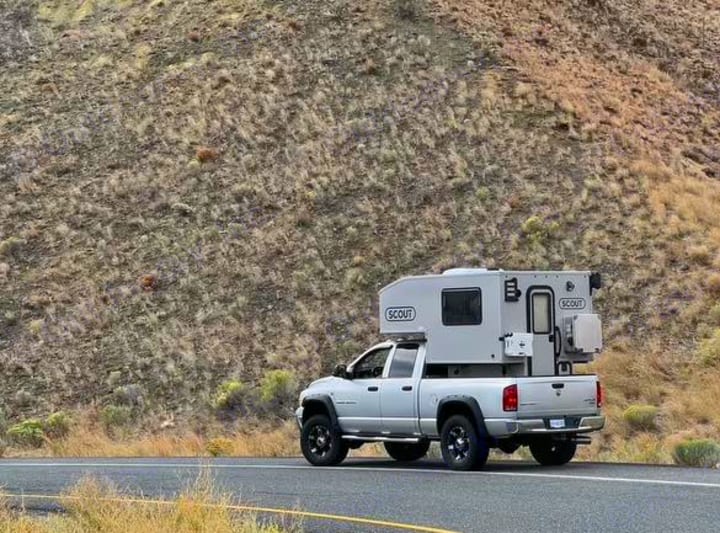 Silver pickup truck with a grey Scout truck camper, parked roadside against a dry hillside. Ideal for an RV rental adventure.. Dodge Dodge Bighorn 3500 Heavy Duty Pu 2005