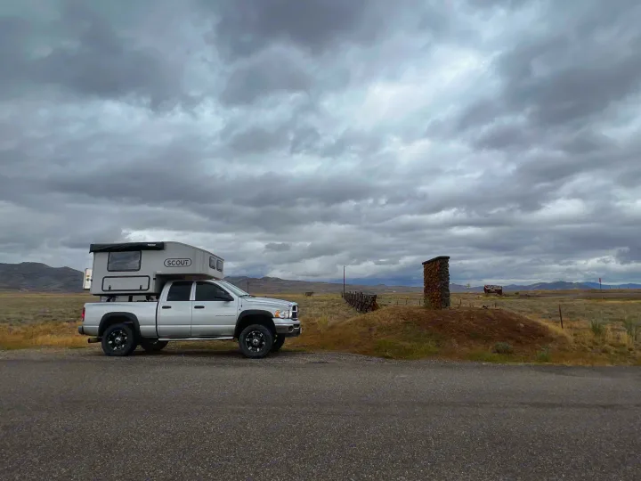 A silver pickup with SCOUT truck camper (RV rental) under cloudy skies in a vast, dry landscape. Ideal for remote travel.. Dodge Dodge Bighorn 3500 Heavy Duty Pu 2005