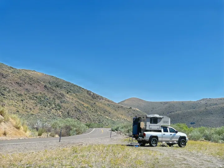 RV rental: A silver pickup with a 'Scout' truck camper parked roadside in dry, rolling hills under a clear sky, ready for adventure.. Dodge Dodge Bighorn 3500 Heavy Duty Pu 2005