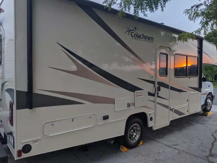 Beige RV rental parked on concrete, reflecting the vibrant sunset in its side windows.. Forest River Coachmen Freelander 2020