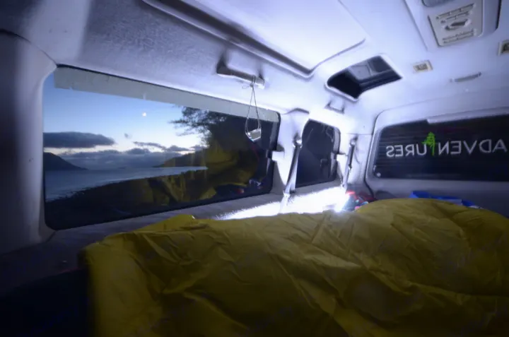Cozy rv rental interior with yellow bedding and a stunning twilight view of a lake and moon, perfect for adventure travel.. MITSUBISHI Delica 1997