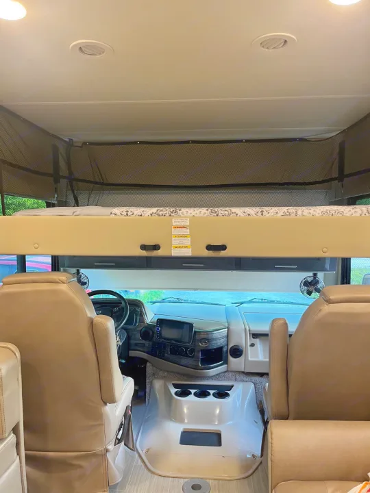 Spacious RV rental interior featuring a cozy overhead bunk and a comfortable cockpit setup for your next adventure.. Thor Challenger 2021