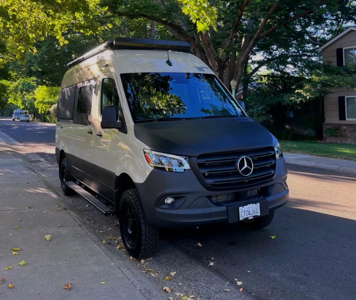 Custom two-tone Mercedes Sprinter camper van, perfect for RV rental adventures, parked under trees on a sunny street.. Winnebago Revel 2023