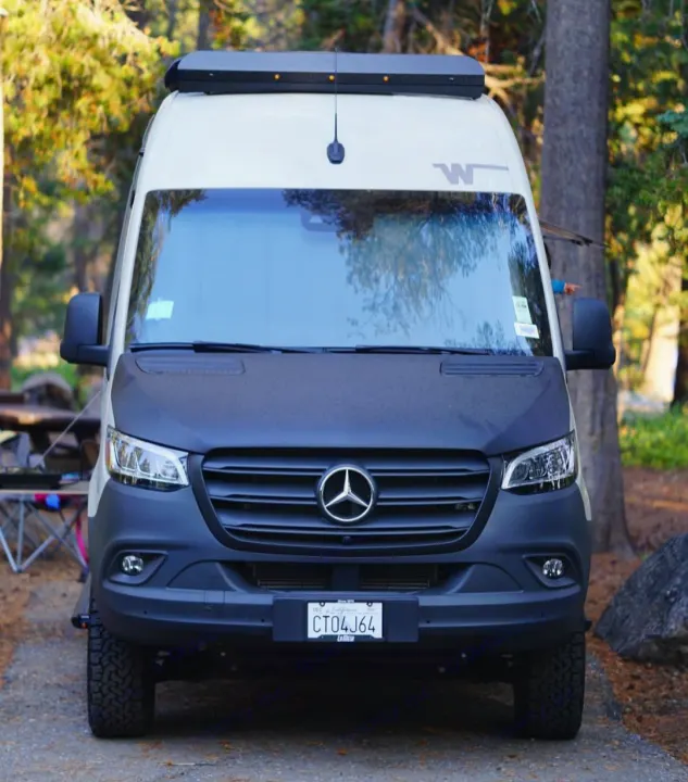 Front view of a sleek white Sprinter van, an RV rental ready for adventure & camping in nature.. Winnebago Revel 2023