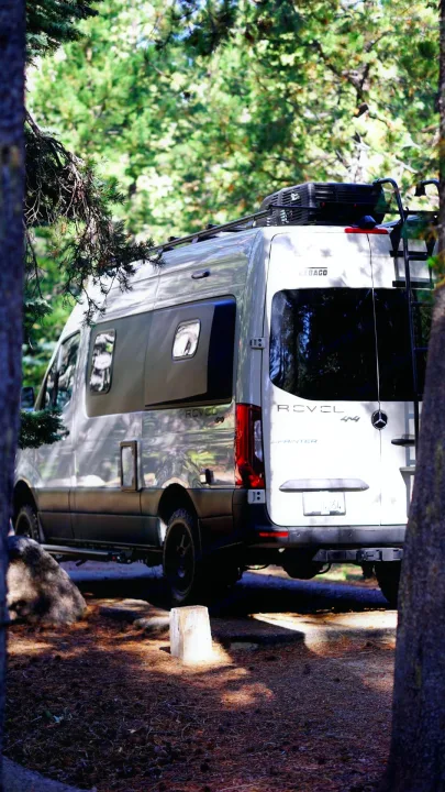 A Winnebago Revel 4x4 camper van, an ideal RV rental for off-grid adventures, parked in a sunny forest.. Winnebago Revel 2023