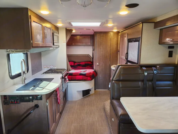 An RV rental interior reveals a cozy kitchen, bedroom with plaid bedding, and dining booth. Compact and ready for travel.. Adventurer 24DS 2020