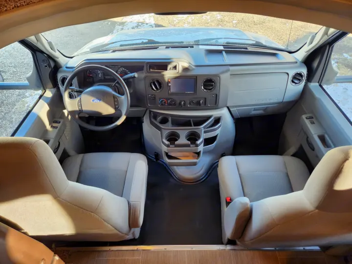 Forward view into an RV rental's cockpit, featuring a Ford steering wheel, dashboard, infotainment, and front seats.. Adventurer 24DS 2020