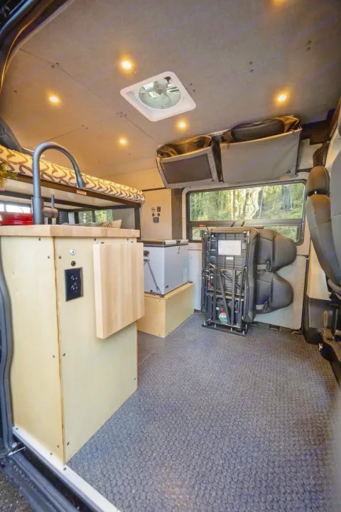 Explore in comfort: RV rental camper van interior with kitchen, bunk bed, portable fridge, storage, and ceiling fan.. Ram ProMaster 2021