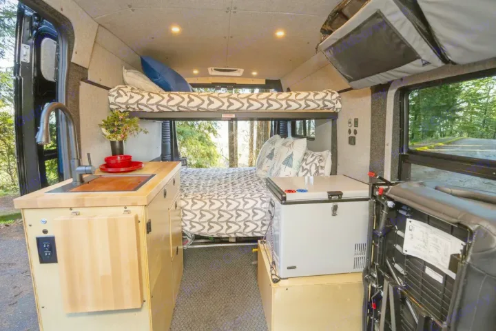 RV rental interior: compact kitchenette, upper & lower beds, and fridge, perfect for comfortable camper van trips.. Ram ProMaster 2021