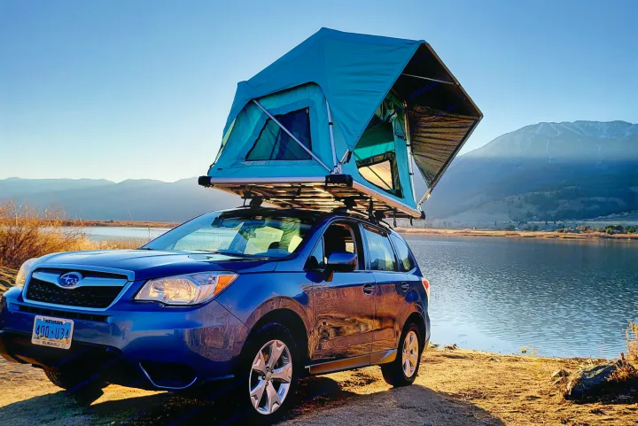 Blue Subaru Forester with rooftop tent deployed by a lake and mountains. A versatile RV rental for nature camping adventures.. Subaru Subaru Forester/Roof Top Tent 2015