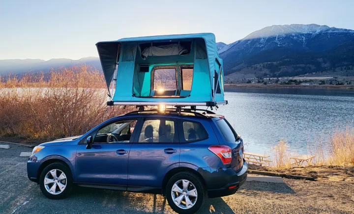 RV rental: Blue Subaru Forester with a rooftop tent parked by a serene lake and snow-capped mountains at sunset.. Subaru Subaru Forester/Roof Top Tent 2015