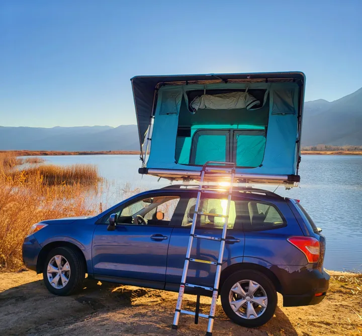 Experience car camping with this Subaru Forester, featuring a rooftop tent by a serene lake. Ideal for your next RV rental getaway.. Subaru Subaru Forester/Roof Top Tent 2015