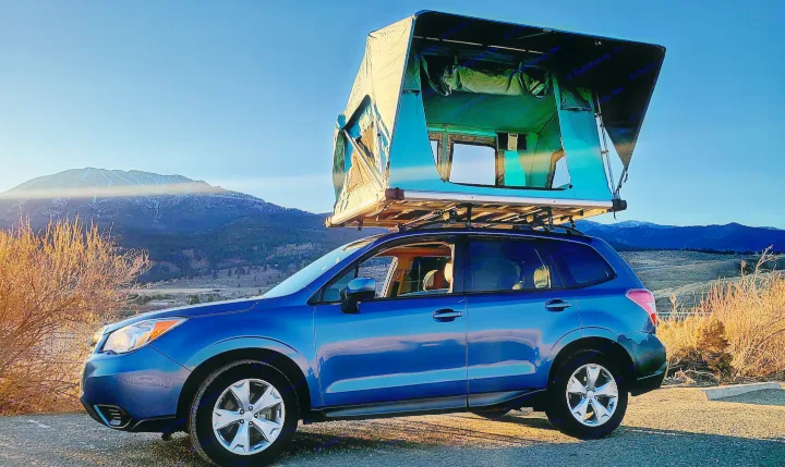 A blue Subaru SUV with a large, deployed rooftop tent, parked facing mountains at sunset. A great "rv rental" alternative for outdoor camping.. Subaru Subaru Forester/Roof Top Tent 2015