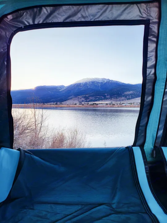 View from inside an RV rental of a vast lake bordered by mountains with patches of snow under a bright sky.. Subaru Subaru Forester/Roof Top Tent 2015